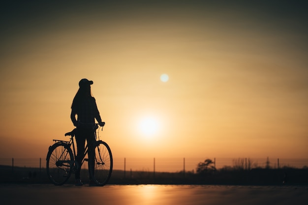 La donna in sella a una bicicletta in città durante il tramonto