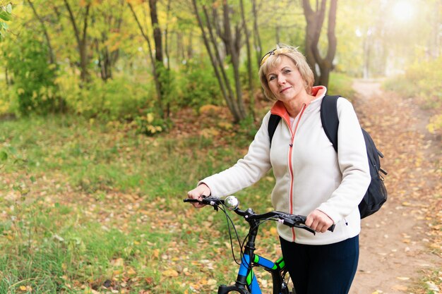 La donna in sella a una bicicletta nel parco. Donna di mezza età che cammina nei boschi. È sulla strada.