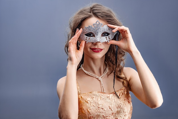 La donna in un abito d&#39;oro e una collana di perle indossa una lucida maschera di carnevale