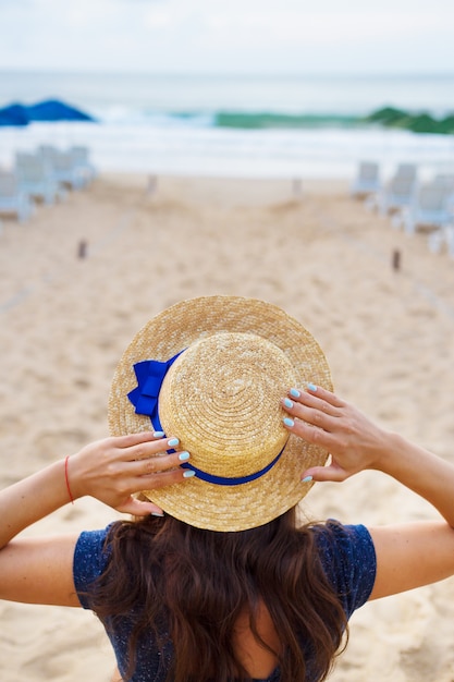 La donna in un cappello si siede su una spiaggia sabbiosa