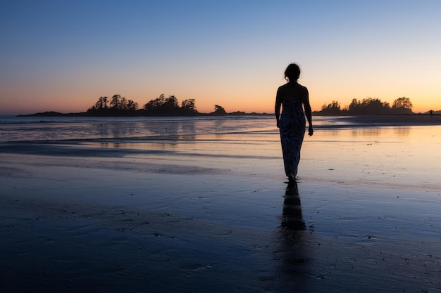 La donna in un vestito casual sta camminando a piedi nudi su una spiaggia sabbiosa dell'oceano verso l'acqua