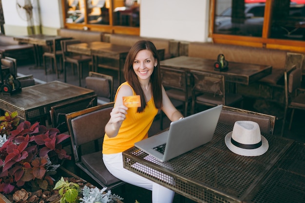 La donna in una caffetteria all'aperto di strada seduta al tavolo con un moderno computer portatile, tiene in mano una carta di credito