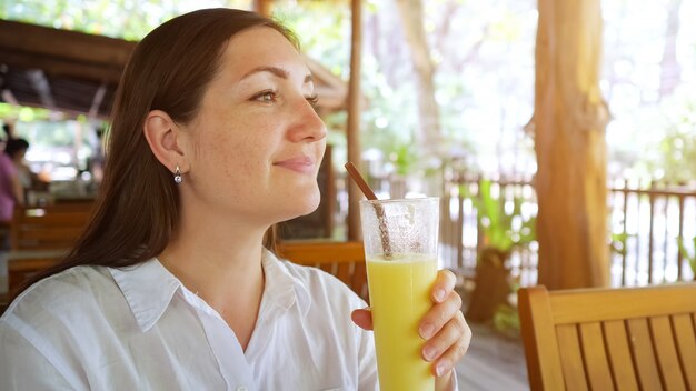 La donna in una camicia bianca beve un frullato.