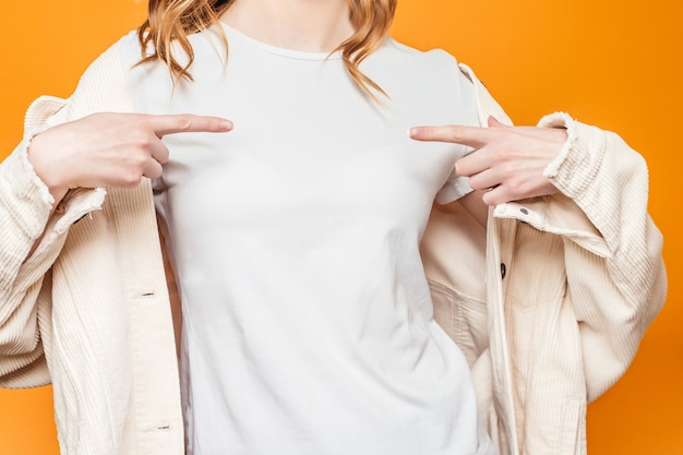La donna in una giacca punta un dito verso una maglietta bianca isolata su uno sfondo arancione