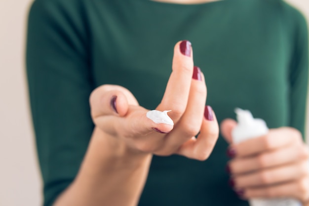 La donna in una maglietta verde e una manicure marrone rossiccio mostra la crema per le mani sul dito