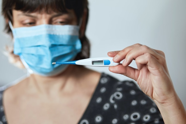 La donna in una maschera legge la temperatura su un termometro