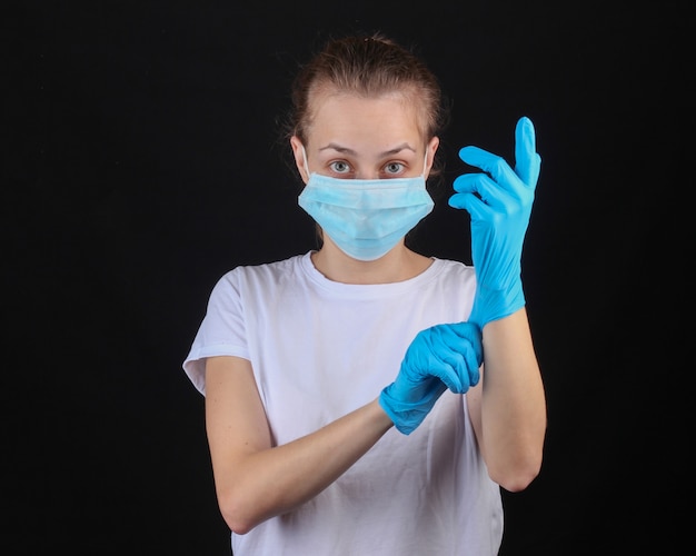 La donna in una mascherina facciale medica copre i guanti su una parete nera. Protezione contro covid-19