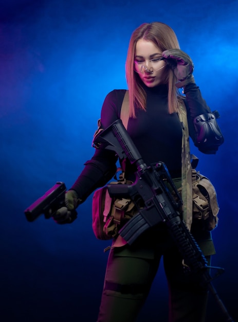 La donna in uniforme militare softair con un fucile automatico americano e una pistola su uno sfondo scuro
