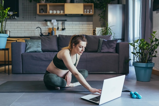 La donna incinta a casa che fa fitness utilizza il laptop per le lezioni online
