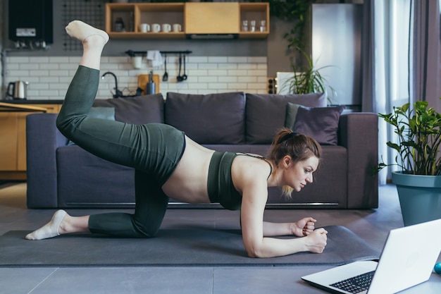 La donna incinta a casa che fa fitness utilizza il laptop per le lezioni online