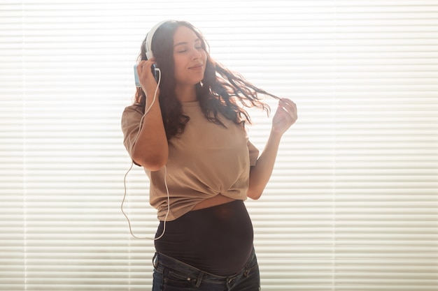 La donna incinta ascolta musica in cuffia a casa e balla, copia spazio.