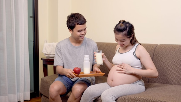 La donna incinta asiatica resta a casa con il marito. Donna che beve latte per la salute e il benessere della gravidanza.