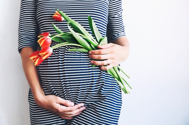 La donna incinta con i fiori dei tulipani tiene le mani sulla pancia Preparazione e aspettativa della gravidanza