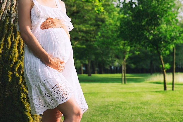 La donna incinta in abito bianco tiene le mani sulla pancia Aspettativa di gravidanza nuovi concetti di vita