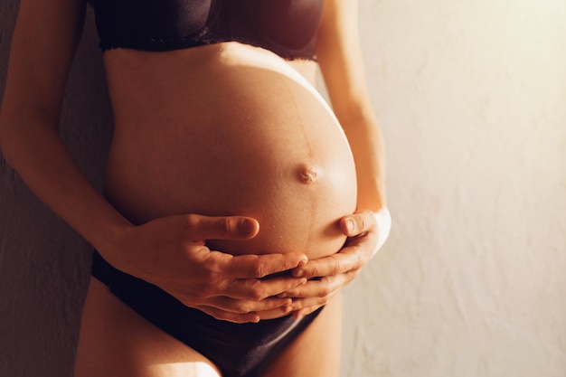 La donna incinta in biancheria intima nera tiene le mani sulla pancia Preparazione alla gravidanza