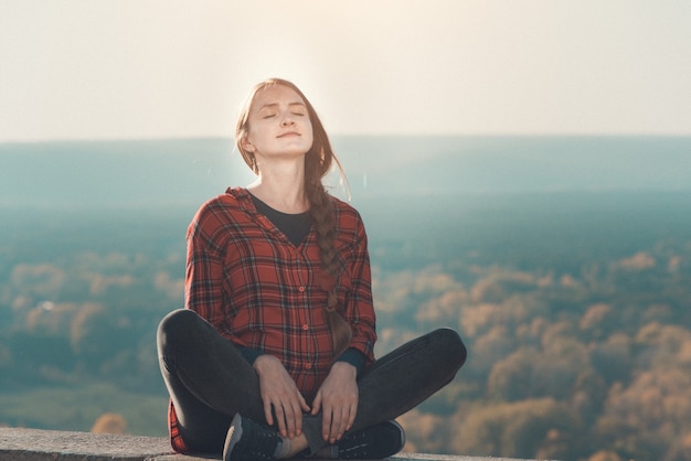 La donna incinta si siede su una collina con gli occhi chiusi. Meditazione. Bosco autunnale sullo sfondo