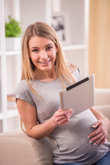 La donna incinta sta tenendo il suo tablet è seduto su un divano.