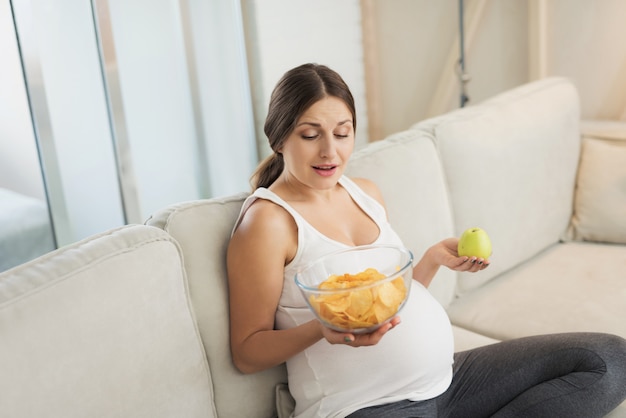 La donna incinta tiene il vaso di patatine fritte e una mela in sue mani