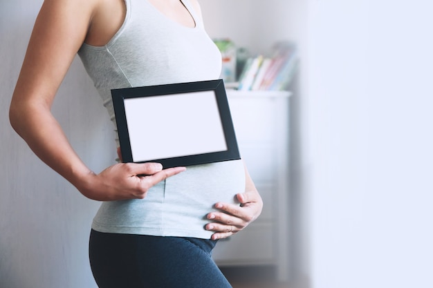 La donna incinta tiene la lavagna vuota del modello per il tuo testo Concetto di gravidanza