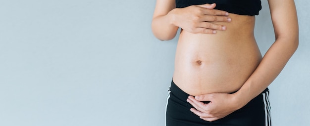 La donna incinta tiene le mani sulla pancia e sullo sfondo color pastello Preparazione alla maternità in gravidanza e concetto di aspettativa Spazio copia primo piano Giovane donna in attesa della nascita del bambino