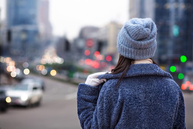 La donna indossa cappotto invernale alla moda e cappello guardando il traffico della città la sera. Spazio per il testo