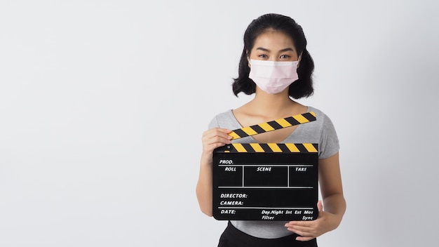 La donna indossa la maschera facciale e le mani che tengono il ciak nero o l'ardesia del film su sfondo bianco