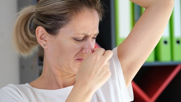 La donna infelice odora la sua ascella da vicino odore sgradevole sotto l'ascella e problema di salute