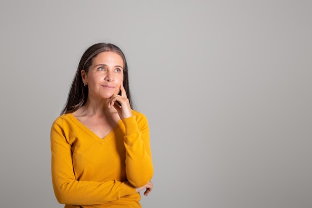 La donna invecchiata caucasica pensierosa positiva che esamina lo spazio della copia pensa che pianifica il giorno