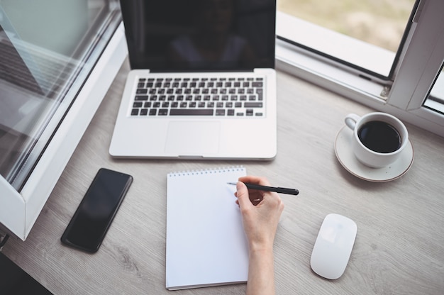 La donna irriconoscibile passa la scrittura in taccuino e computer vuoti. Libero professionista che utilizza smartphone e laptop a casa durante la quarantena. Internet marketing, finanza, affari, concetto di lavoro a distanza