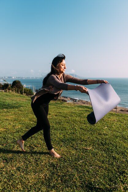 La donna lancia la sua stuoia sull'erba per fare yoga all'aperto