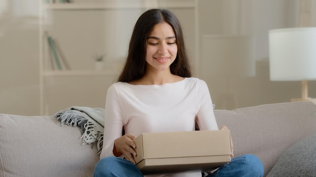 La donna latina araba sorpresa cliente soddisfatto shopaholic si siede sul divano a casa pacco di consegna aperto