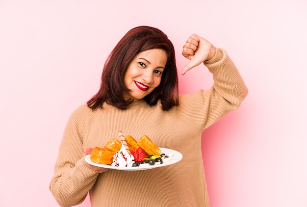 La donna latina di mezza età con in mano un waffle si sente orgogliosa e sicura di sé, esempio da seguire.