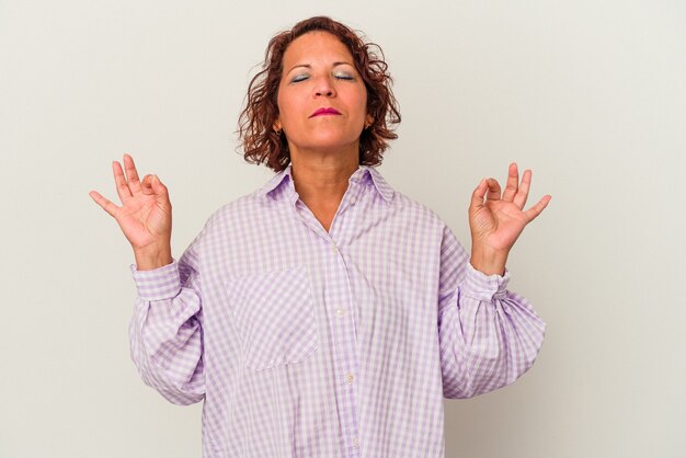 La donna latina di mezza età isolata su sfondo bianco si rilassa dopo una dura giornata di lavoro, sta eseguendo yoga.