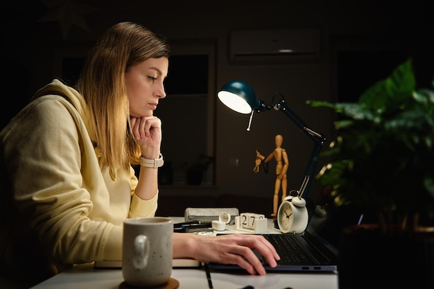 La donna lavora a casa in ufficio di notte utilizzando il computer portatile