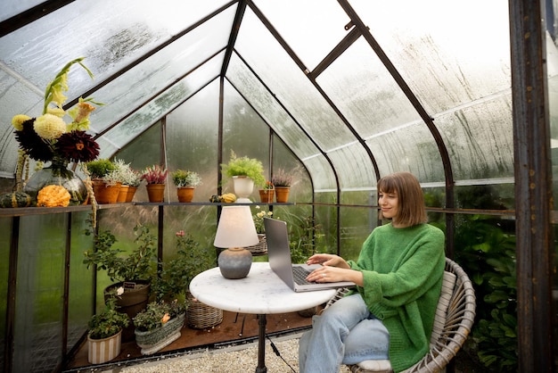 La donna lavora a distanza sul computer portatile in serra nel cortile