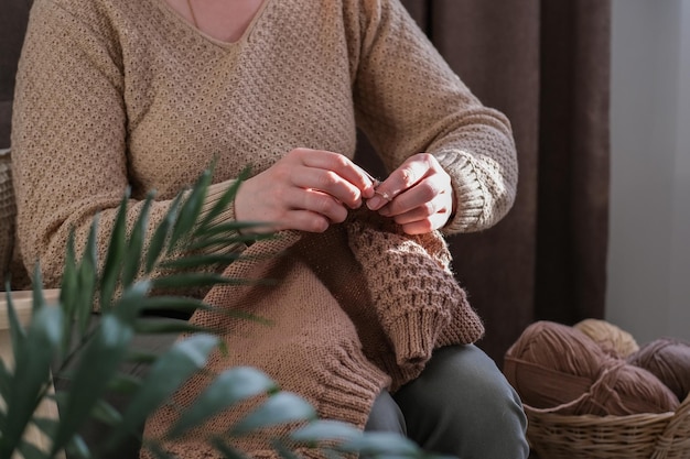 La donna lavora a maglia un maglione di lana su ferri da maglia Accessori nelle vicinanze per lavorare a mano in cesto di vimini