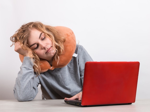 la donna lavora al computer con il cuscino intorno al collo su bianco.