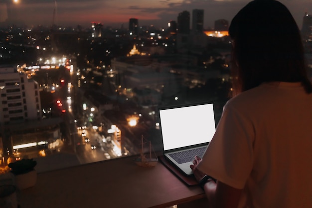 La donna lavora con il laptop vicino all'appartamento di Windows con vista sulla città di sera