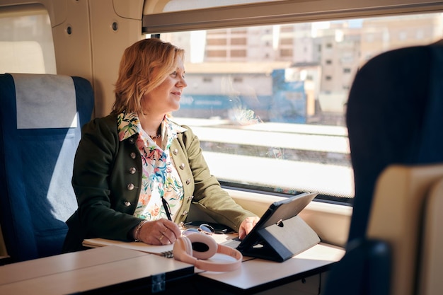 La donna lavora da un treno con un tablet e un notebook Lavorando in remoto viaggiare