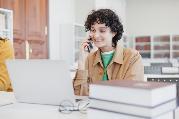 La donna lavora in biblioteca coworking al computer portatile e parla al telefono ricercatore all'università