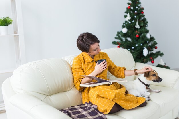 La donna legge il libro davanti all'albero di Natale con il cane jack russell terrier