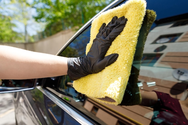 La donna lucida l'auto usa un panno in microfibra e un lucido per pulire la carrozzeria dell'auto con lo smalto