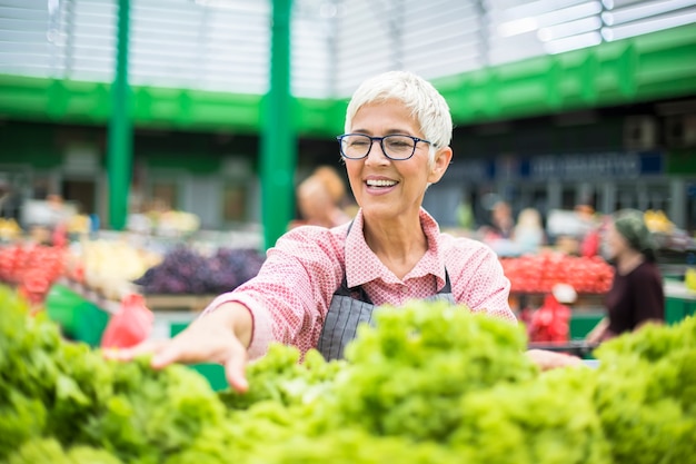 La donna maggiore vende la lattuga sul mercato