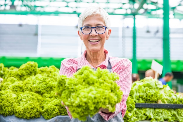 La donna maggiore vende la lattuga sul mercato