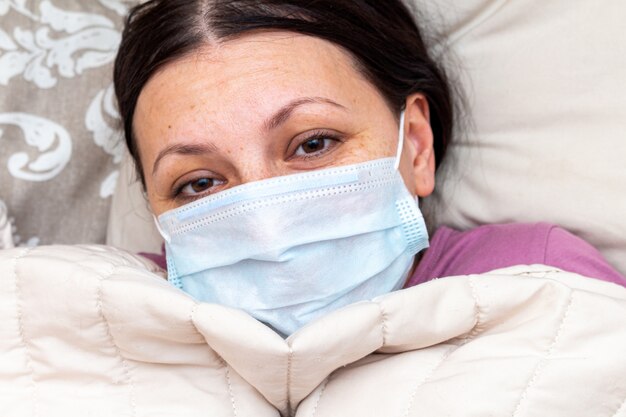 La donna malata soffre di influenza virale a letto in una maschera medica