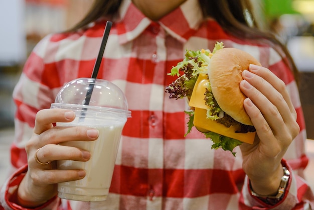 La donna mangia l'hamburger e beve il milk shake da vicino
