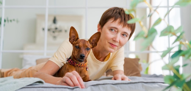 La donna matura si trova sul pavimento con il pinscher miniatura del cane da slitta