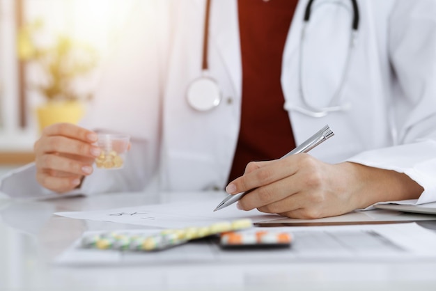 La donna-medico sconosciuta riempie il modulo di prescrizione nella stanza soleggiata, primo piano.