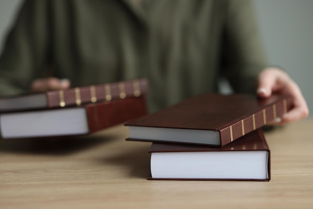 La donna mette spessi libri di storia con copertina rigida marrone sul tavolo di legno il bibliotecario dà materiale