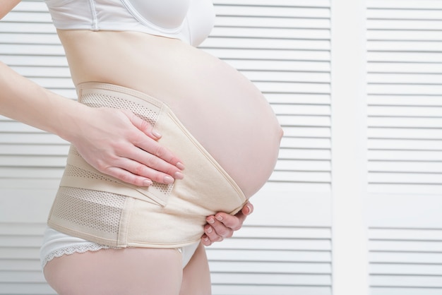 La donna mette una benda per le donne in gravidanza. Avvicinamento.